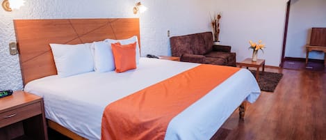 A hotel room with a large bed, wooden headboard, and a nightstand with a lamp.