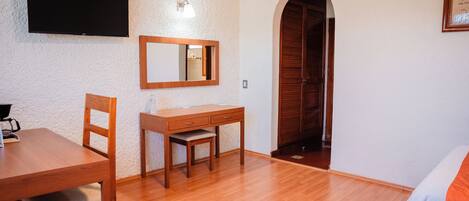 A room with a wooden desk, chair, and a television mounted on the wall.
