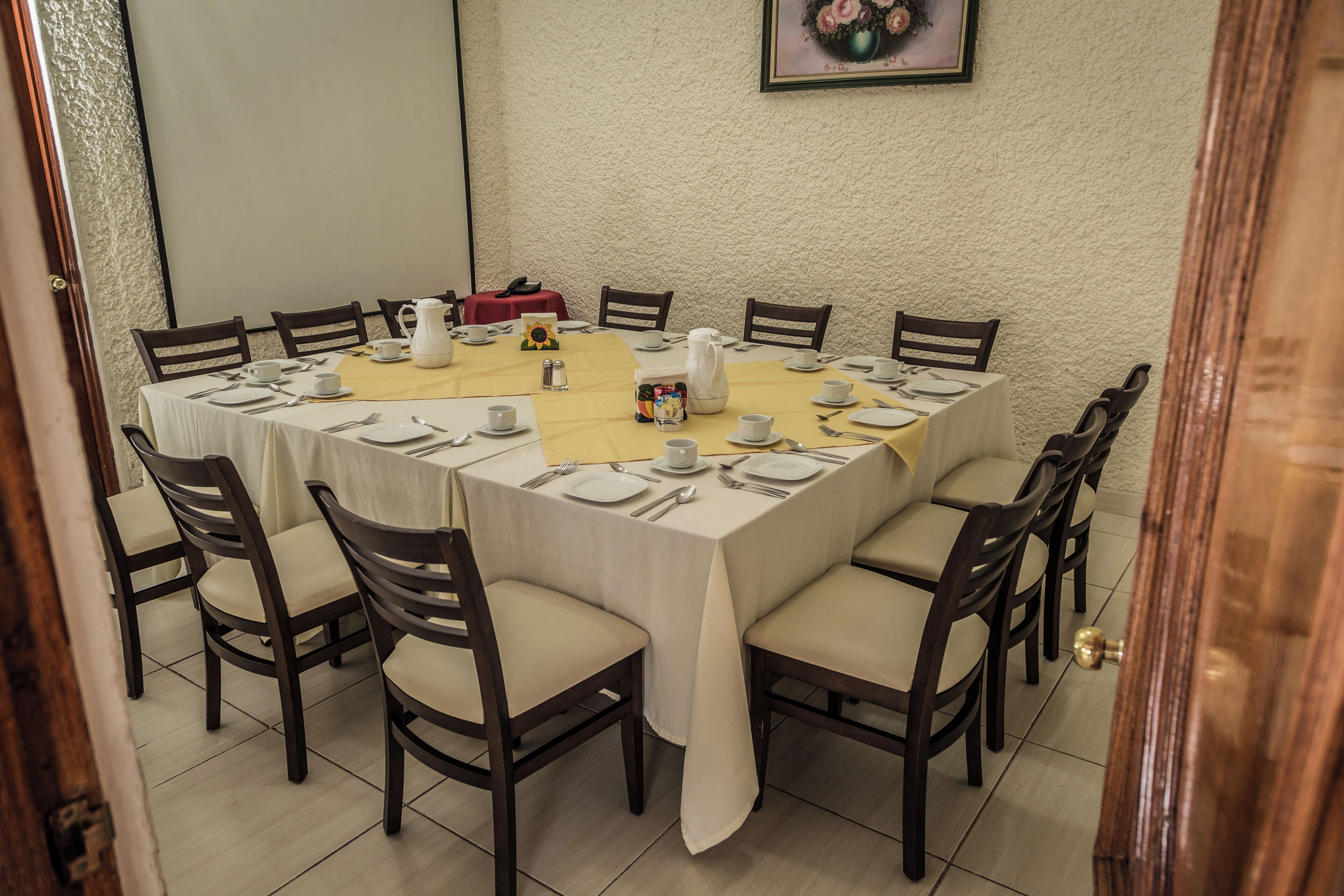 A dining room with a large rectangular table set for a meal, surrounded by chairs.