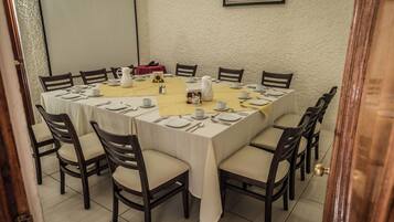 A dining room with a large rectangular table set for a meal, surrounded by chairs.