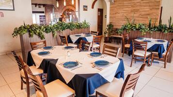 Ein Restaurant mit runden Tischen, Holzsesseln und grünen Pflanzen an den Wänden.