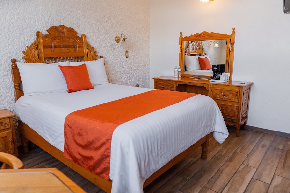 A neatly made bed with a wooden headboard, a bedside table with a lamp, and a mirror on the wall.
