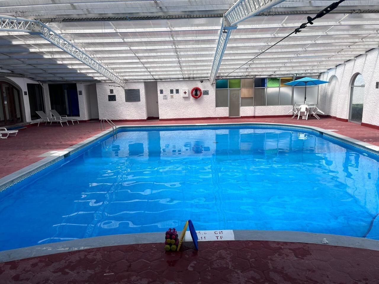 Une piscine intérieure avec un sol rouge, une bouée de sauvetage et un panneau indiquant la profondeur.