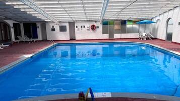 Une piscine intérieure avec un sol rouge, une bouée de sauvetage et un panneau indiquant la profondeur.