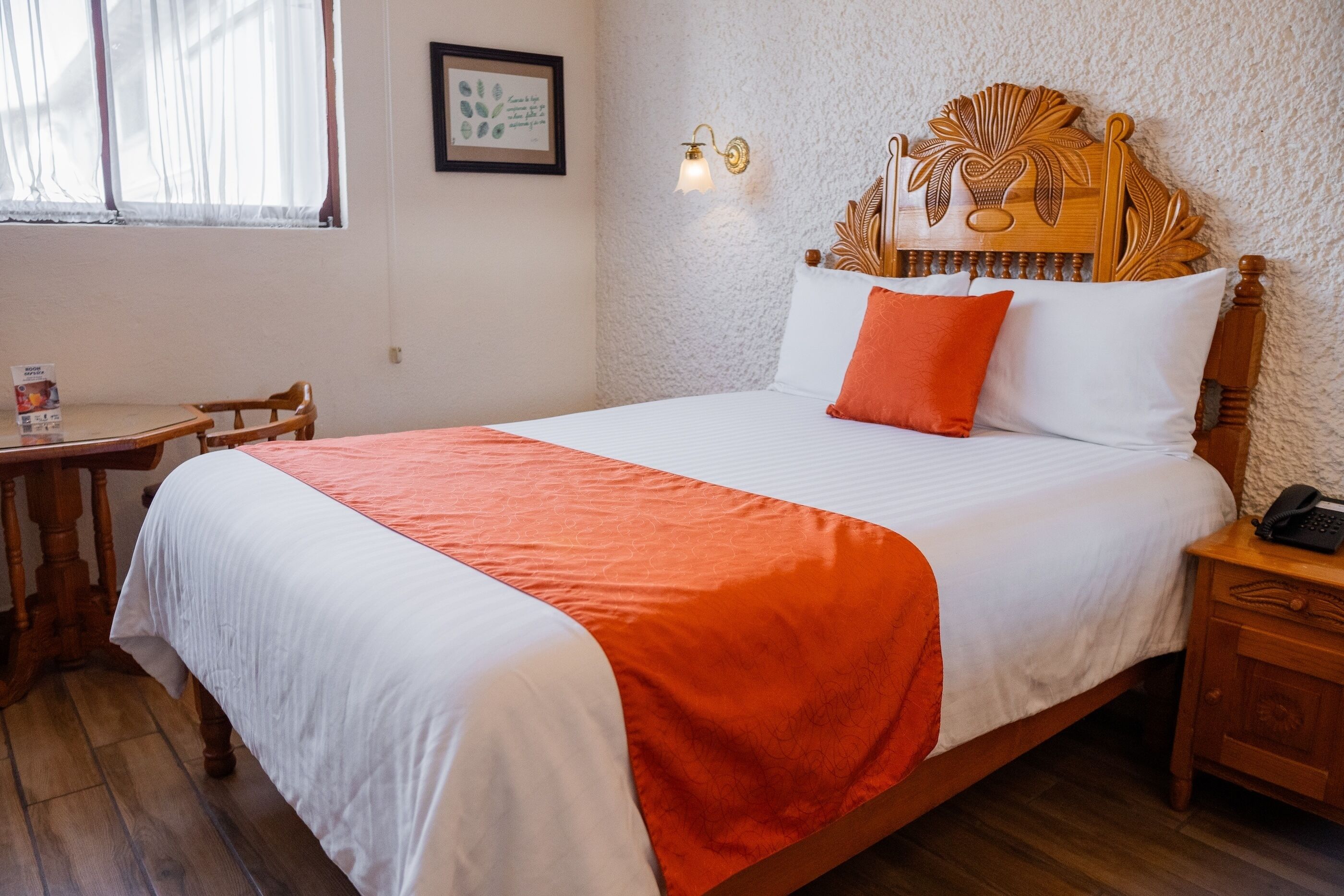 A neatly made bed with a wooden headboard, a bedside table with a lamp, and a framed picture on the wall.