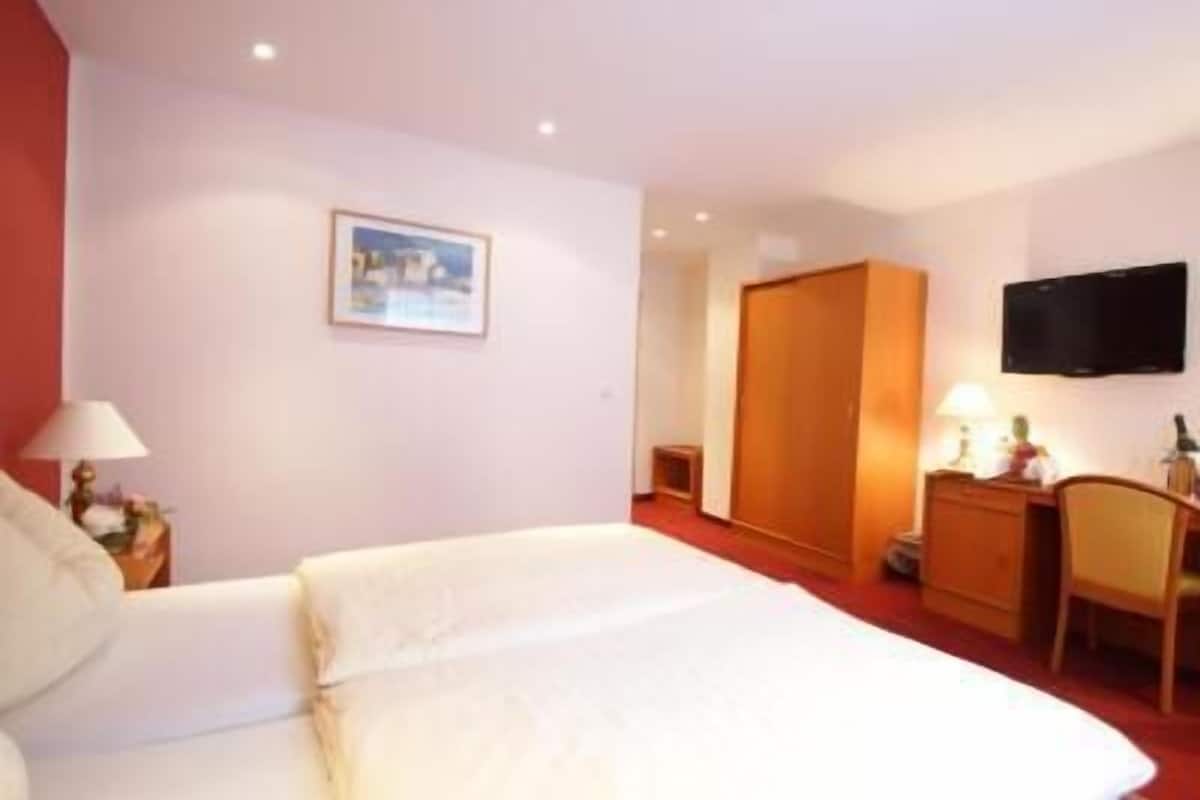 A hotel room with a bed, a desk, a chair, a wardrobe, a television, and a picture on the wall.