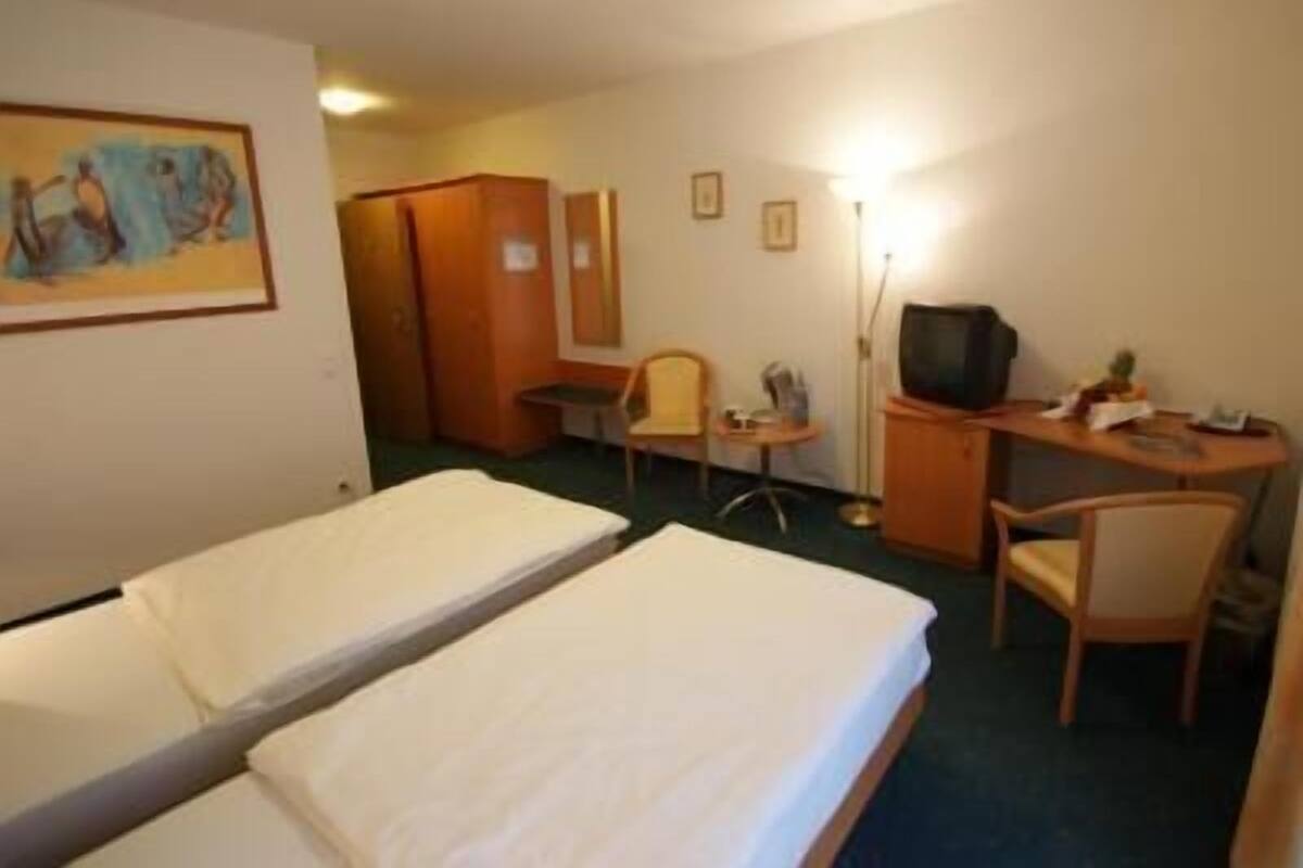 A hotel room with two single beds, a desk with a chair, a television, and a small table.