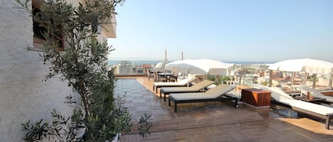 A rooftop terrace with lounge chairs, umbrellas, and a view of the cityscape.