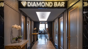 A hallway leading to a 'DIAMOND BAR' with a modern design, marble flooring, and a potted orchid on a console table. - Hotel Grand Washington (Istanbul)