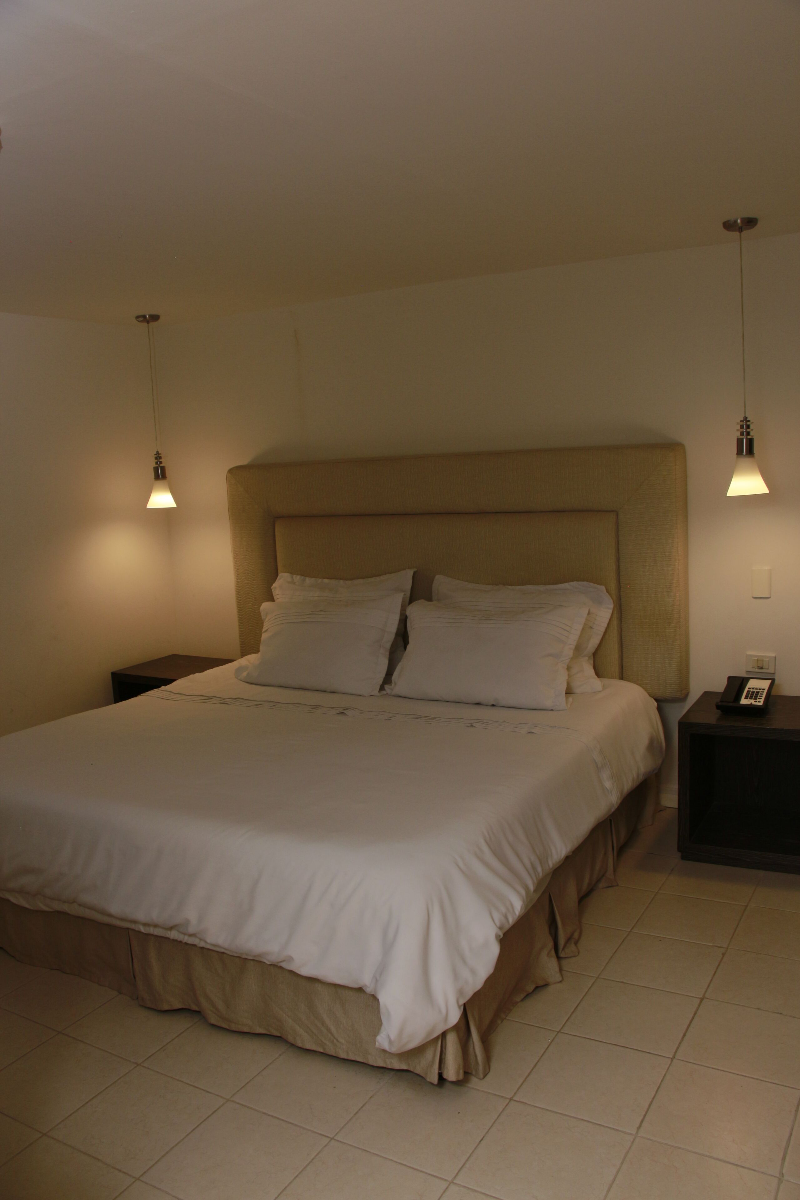 A neatly made bed with a headboard, two bedside tables, and a wall-mounted telephone.