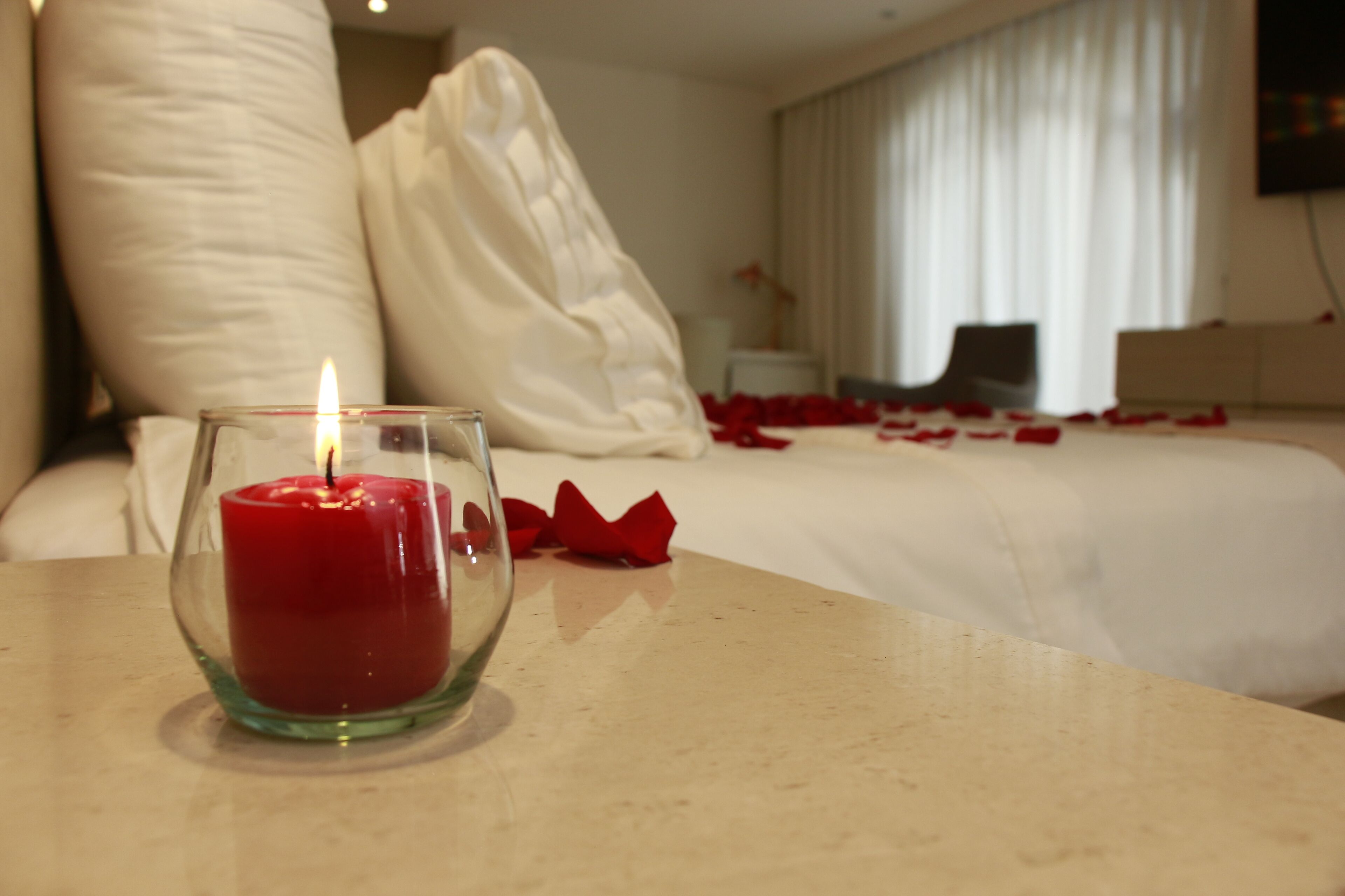 A candle on a table in a hotel room with a bed and pillows.