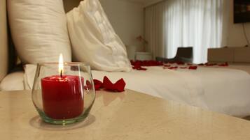 A candle on a table in a hotel room with a bed and pillows.