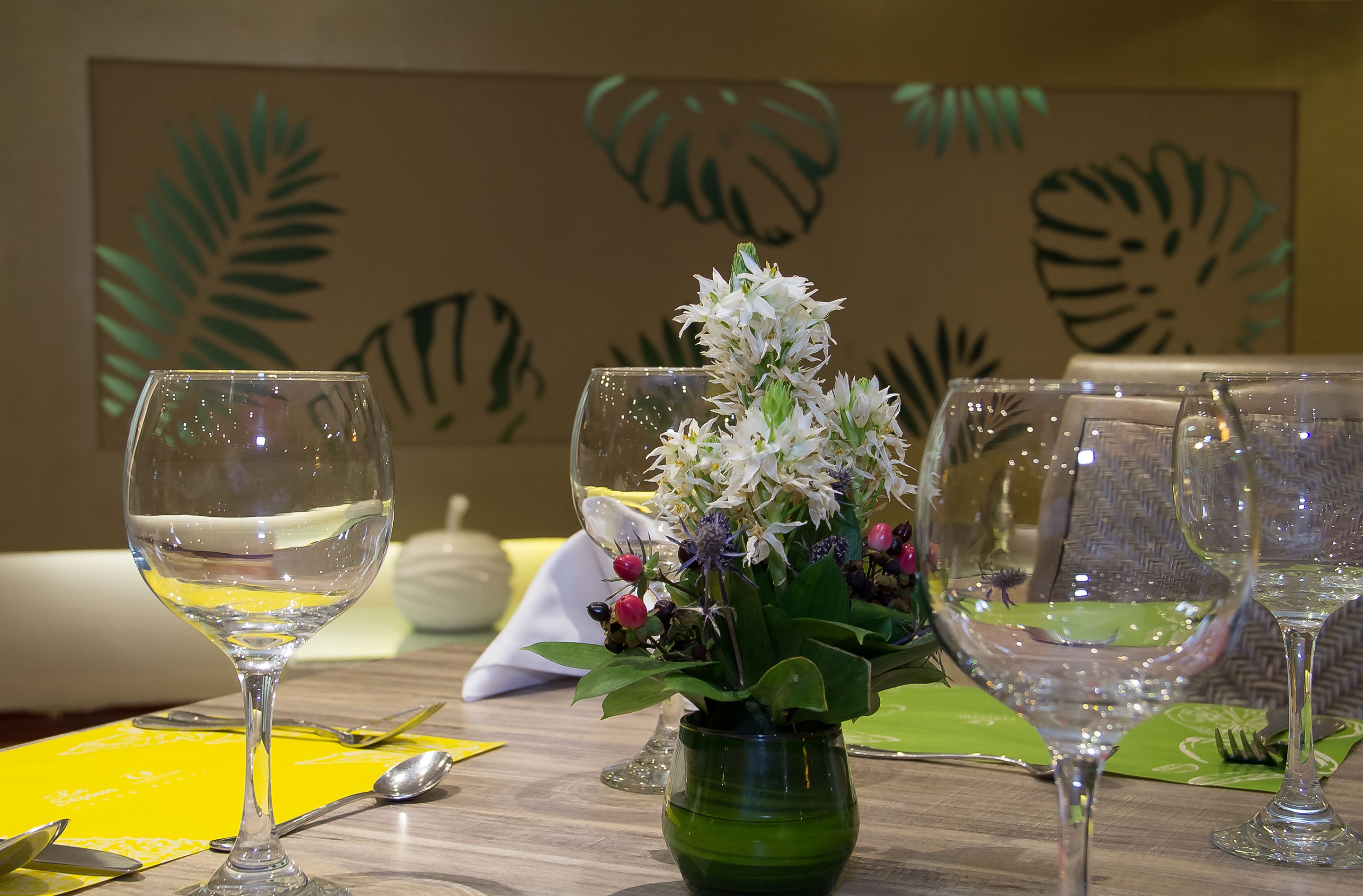 A dining table with empty wine glasses, a green vase with white flowers, and a yellow placemat.