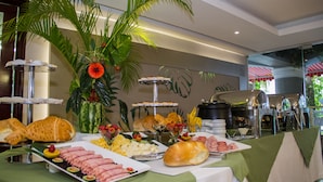 A buffet with various food items, including meats, cheeses, and pastries, with a decorative palm plant and a water feature in the background.