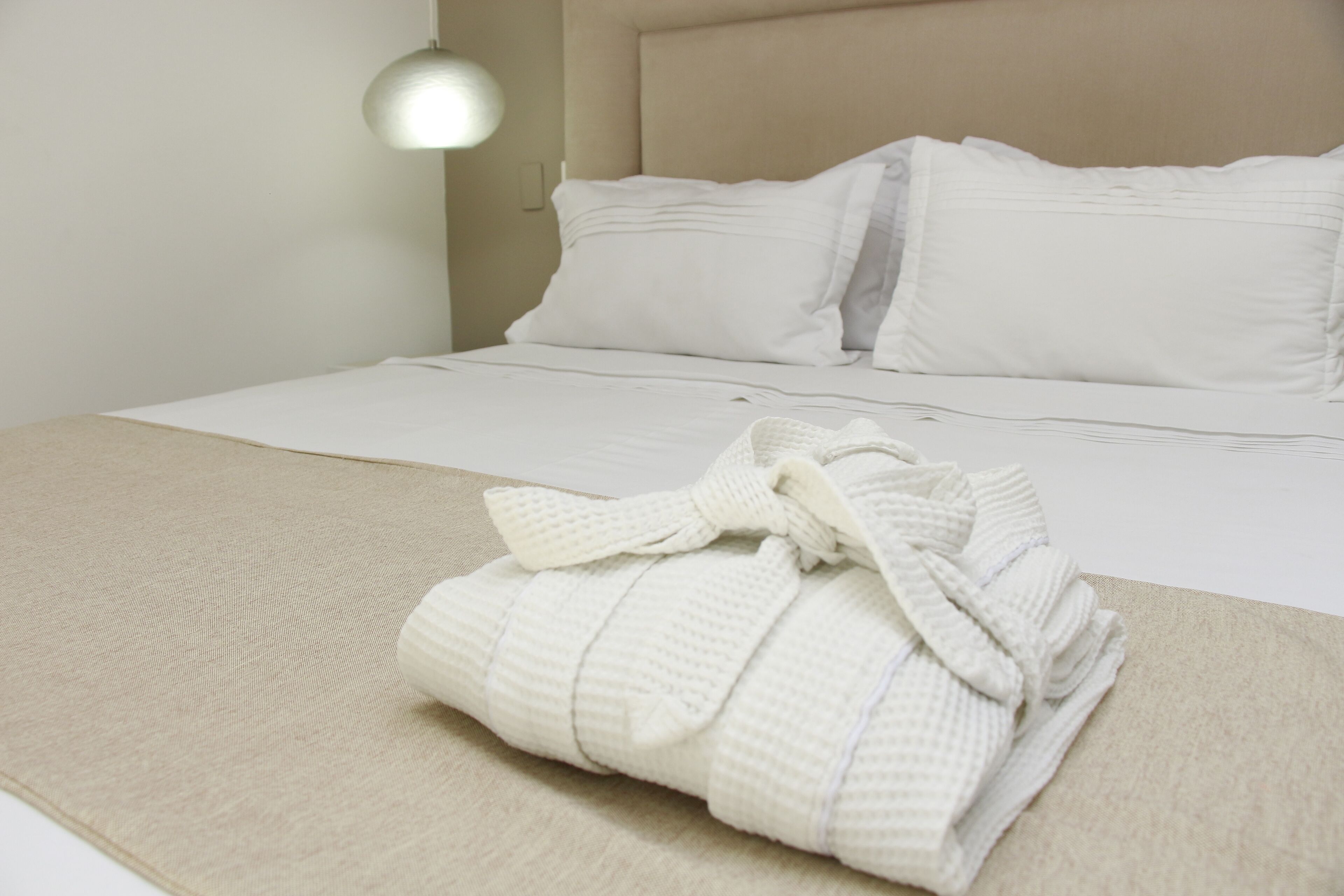 Una cama bien hecha con ropa de cama blanca y una bata doblada sobre la cama.