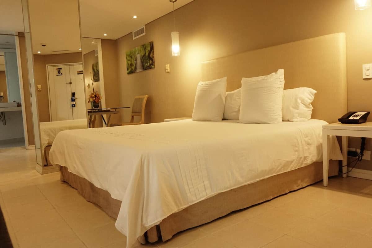 A hotel room with a large bed, a bedside table with a phone, a chair, and a small table with a vase of flowers.