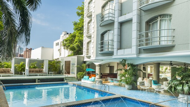 A swimming pool area with lounge chairs and umbrellas, surrounded by a building with balconies and large windows.