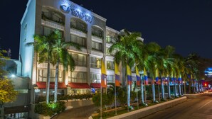 A multi-story hotel with a prominent 'Country Inn' sign, featuring balconies with plants, a red awning, and a row of palm trees in front.