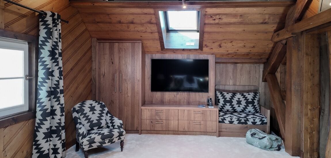 Una habitación acogedora con televisión, dos sillones estampados, una mesita y una ventana.