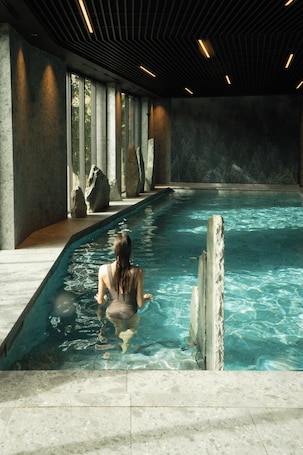 A pool area with a person sitting at the edge, large rocks, and a modern ceiling design.