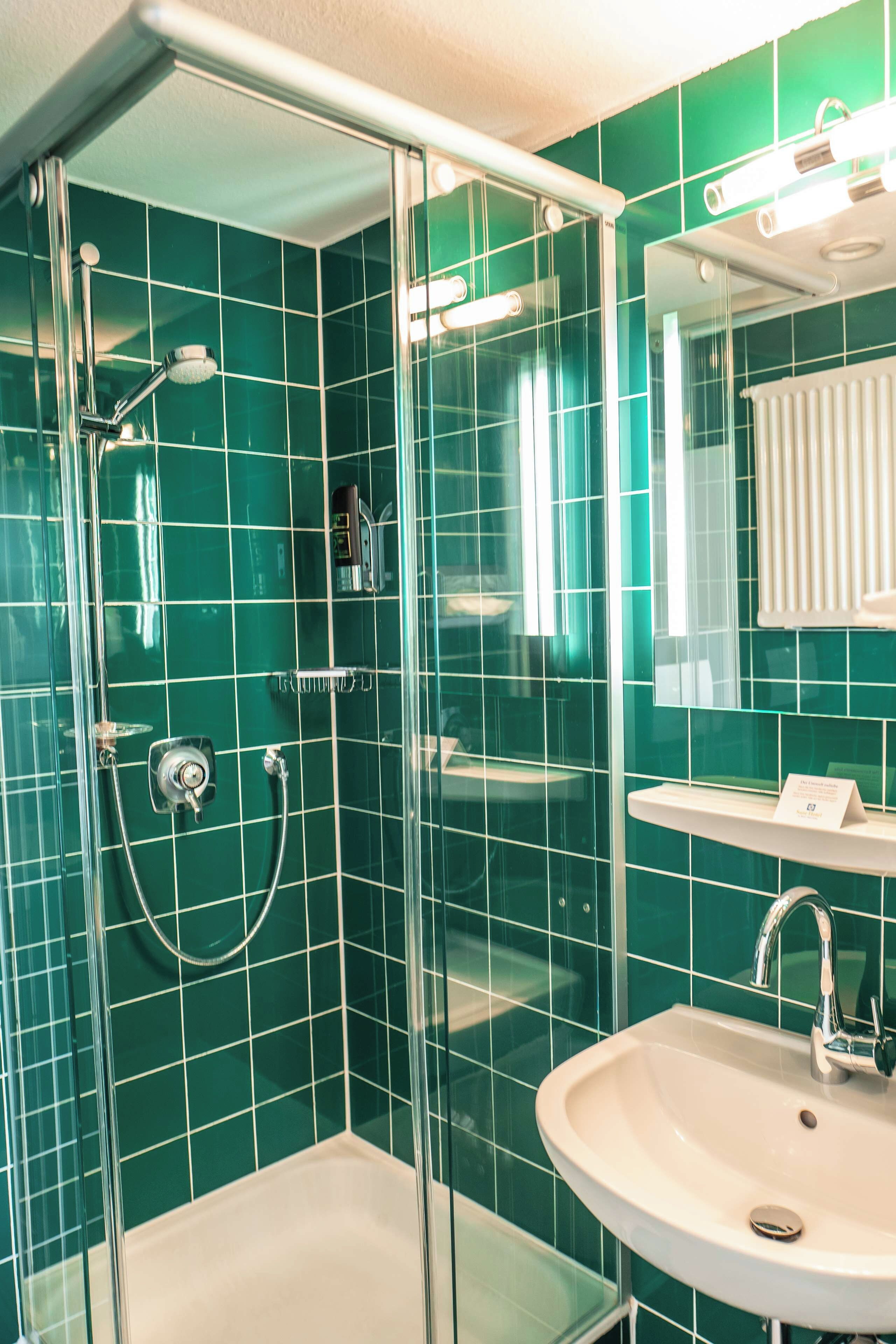 A bathroom with green tiles, a glass-enclosed shower, a sink, and a mirror.