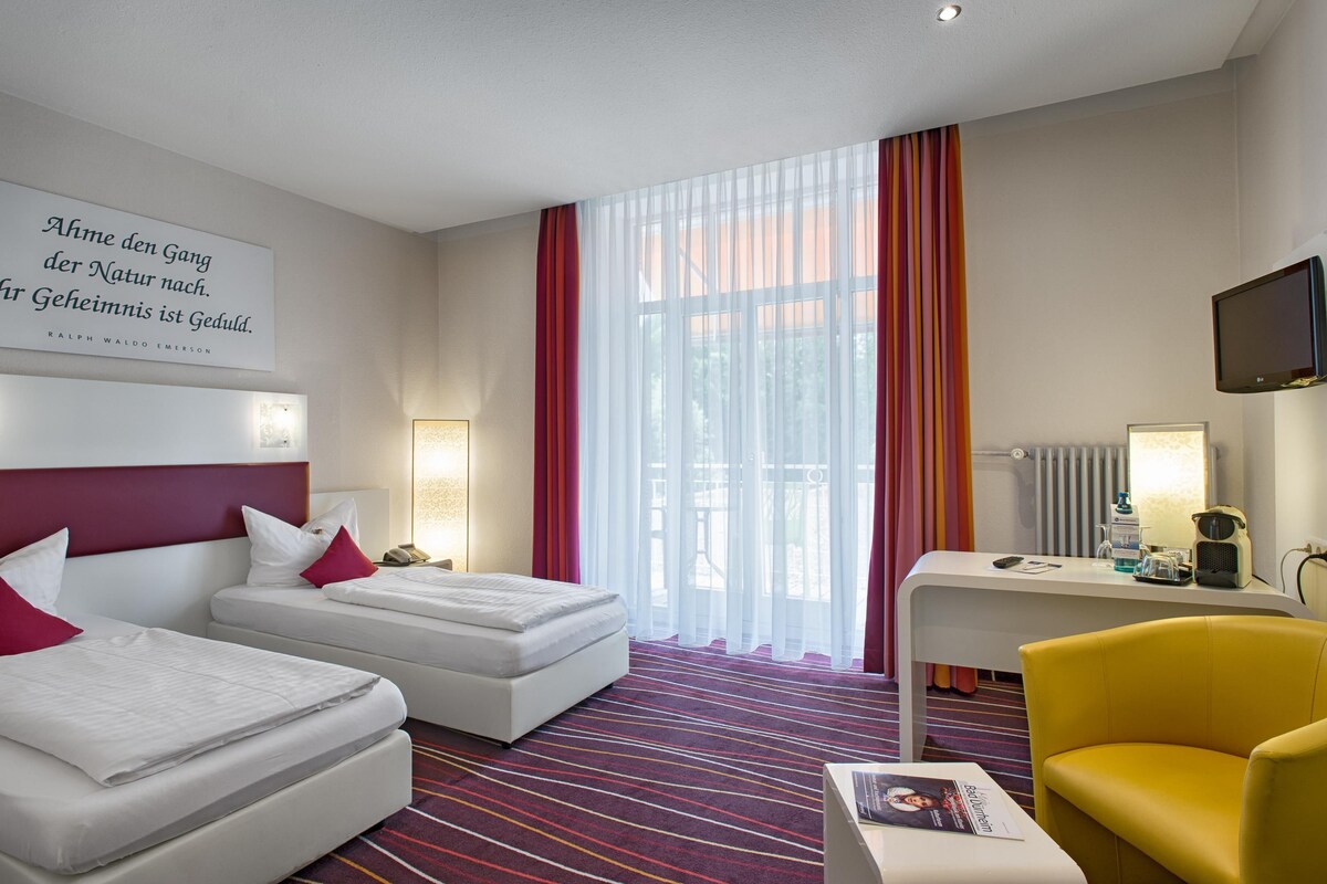 A hotel room with a bed, a desk, a chair, a TV, and a window with curtains.
