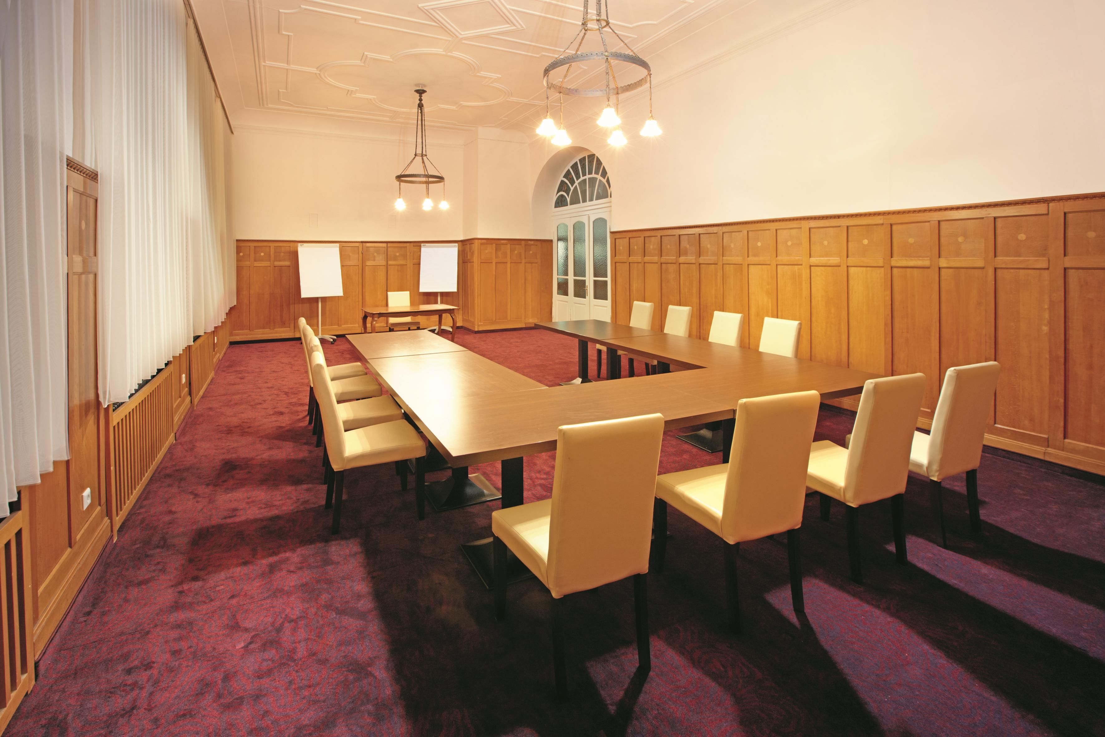 Uma sala de conferências com uma mesa comprida, várias cadeiras, um quadro branco e um candelabro.