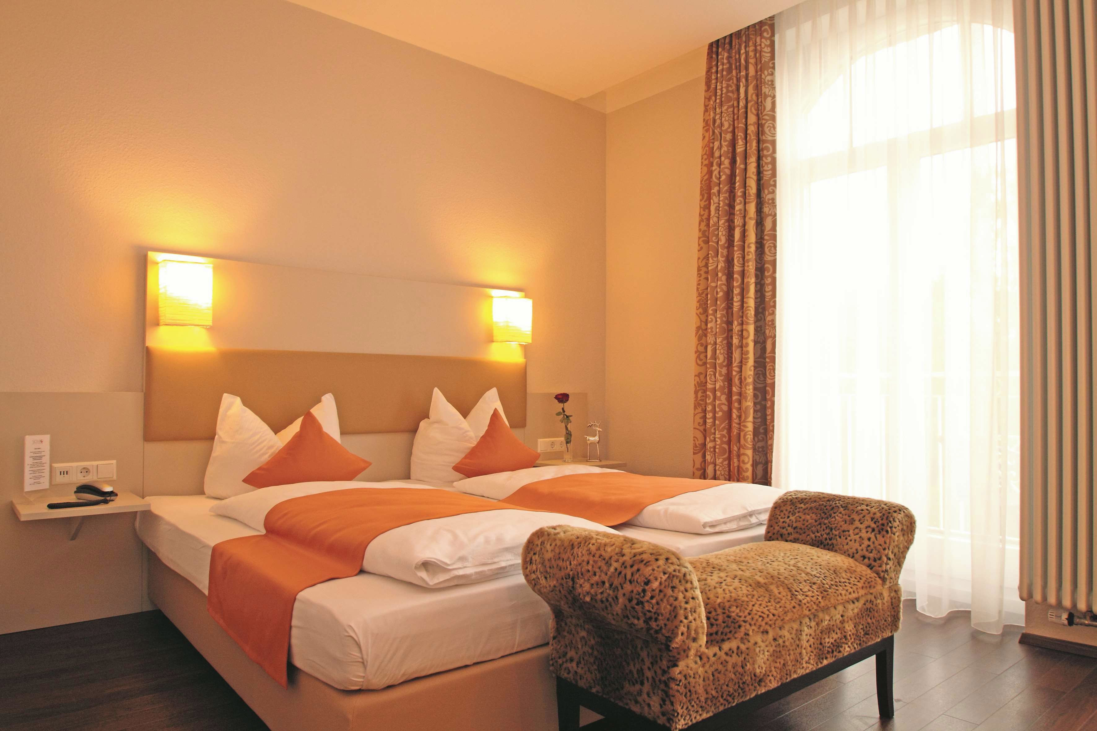 Ein Hotelzimmer mit einem Bett, zwei Nachttischlampen, einem Sessel, einem Nachttisch und einem Fenster mit Vorhängen.