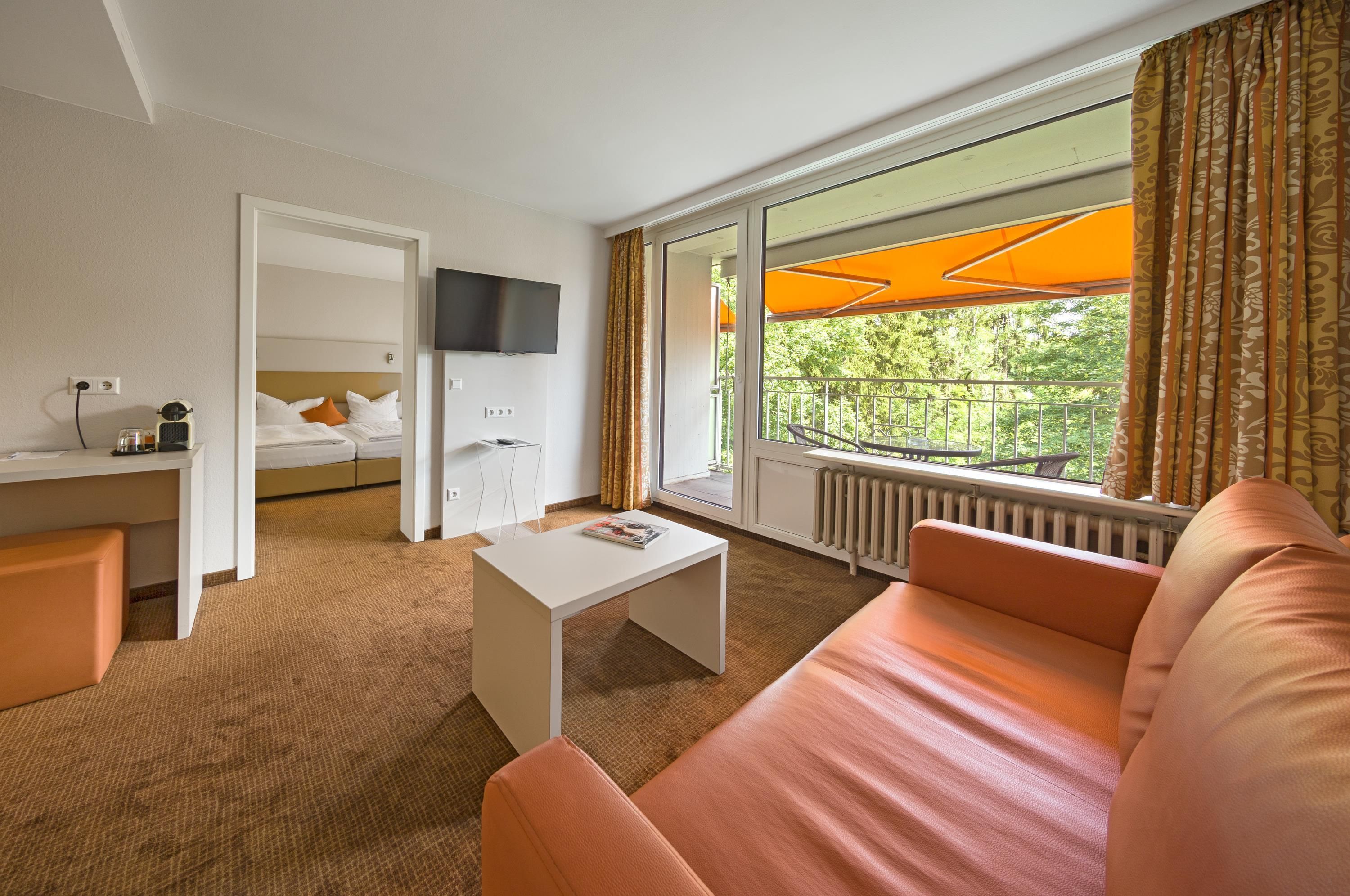 A hotel room with a bed, a TV, a sofa, a coffee table, and a window with curtains.
