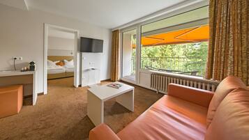 A hotel room with a bed, a TV, a sofa, a coffee table, and a window with curtains.