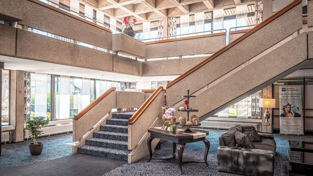 Un vestíbul ampli amb una escala central, una recepció i una zona de seients amb una catifes estampada.
