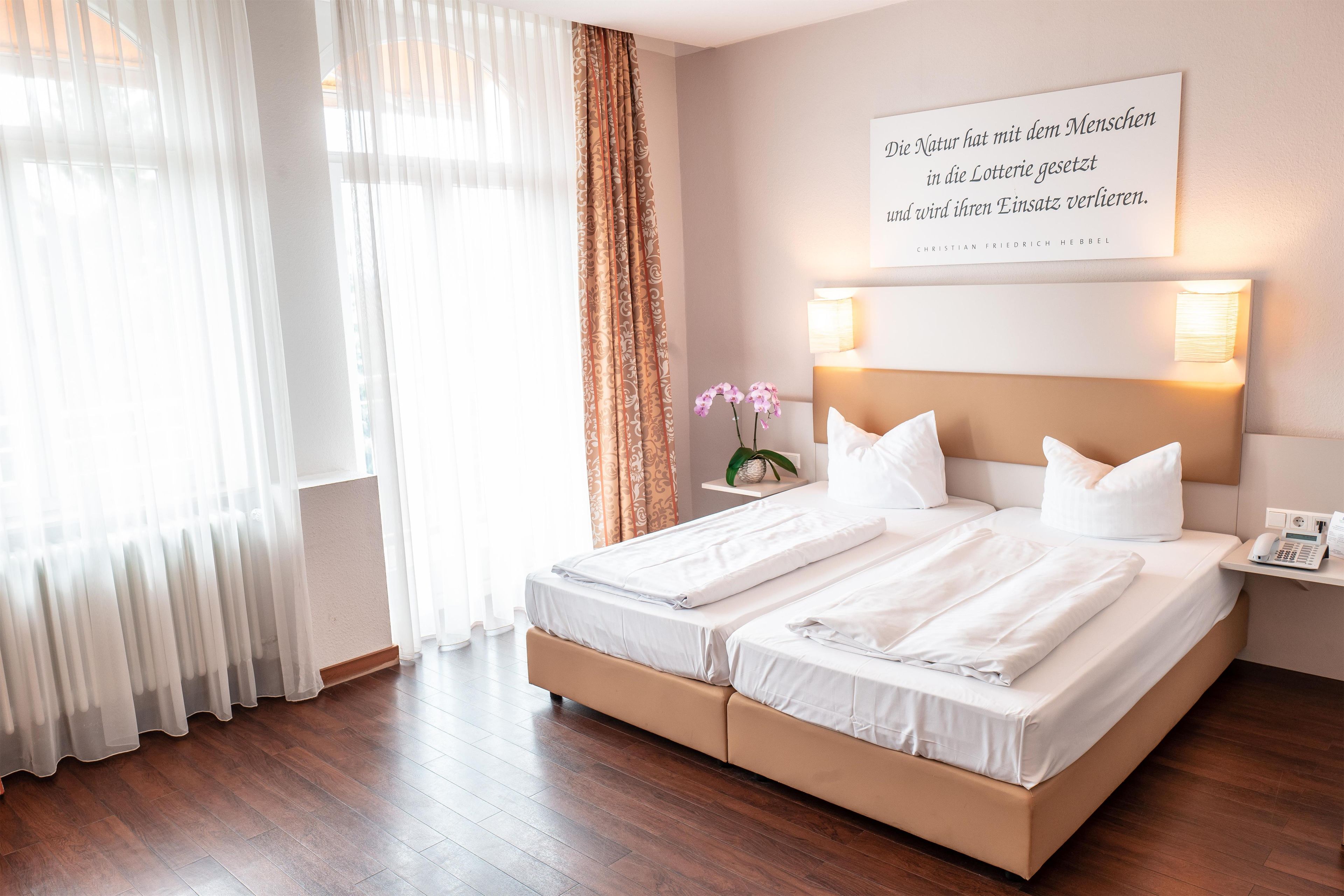 A hotel room with a double bed, a bedside telephone, and a wall-mounted light fixture.