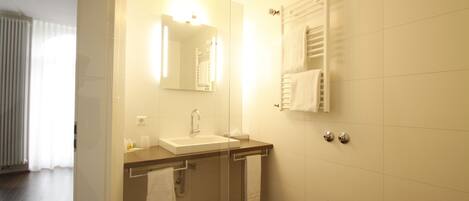 Un baño moderno con mampara de vidrio, lavamanos, espejo y toallero.
