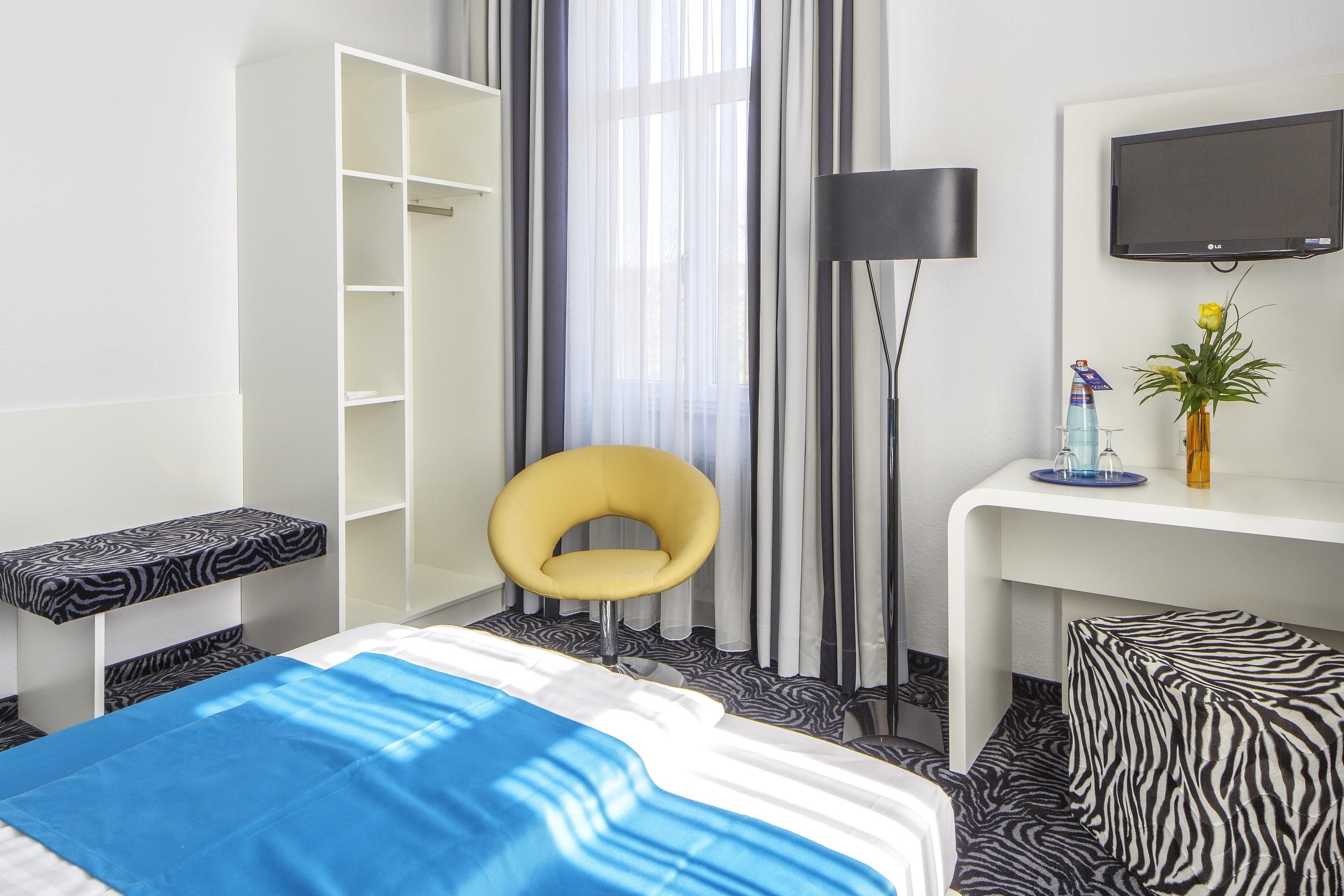 A hotel room with a bed, a chair, a desk, a wardrobe, a television, and a window with curtains.