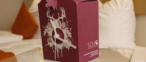 Una caja color burdeos con diseño de reloj y el nombre de un hotel sobre una mesa de vidrio.
