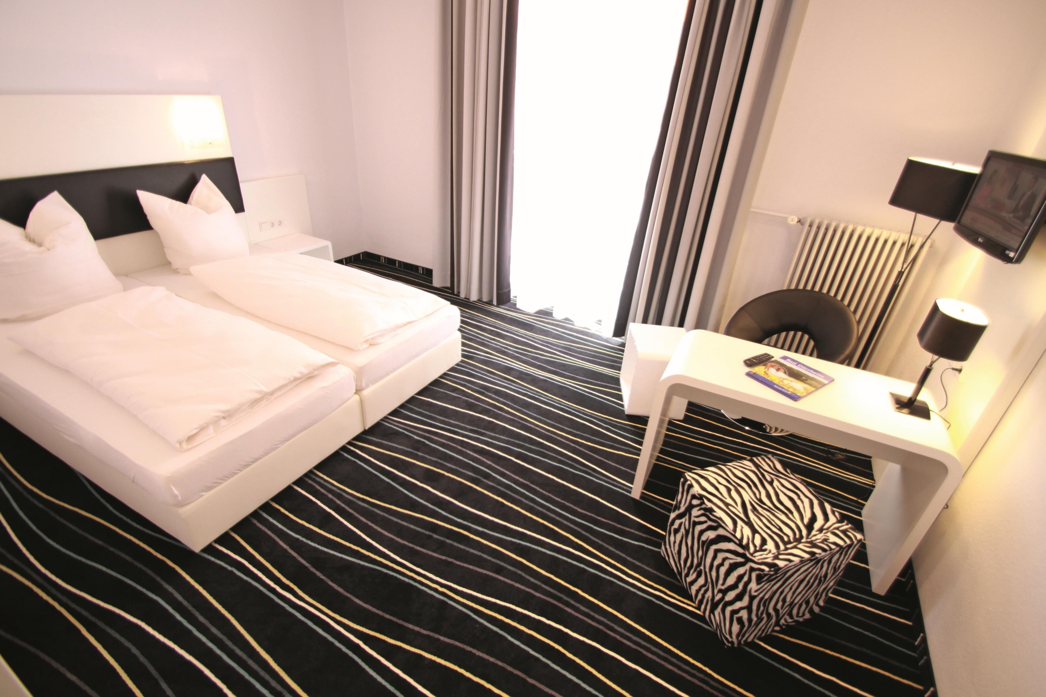 A hotel room with a bed, a desk, a chair, a zebra-patterned ottoman, and a television.