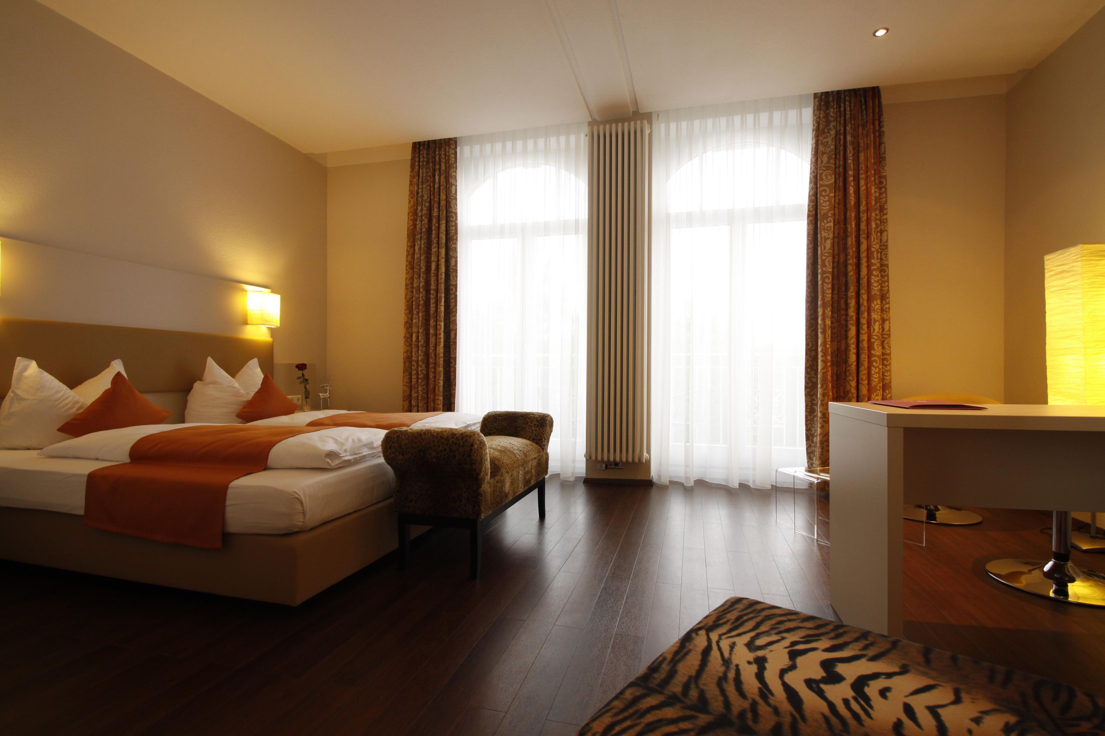A hotel room with a bed, a chair, a desk, and a window with curtains.