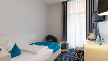 Habitación de hotel con cama, escritorio, silla, televisor y ventana con cortinas.