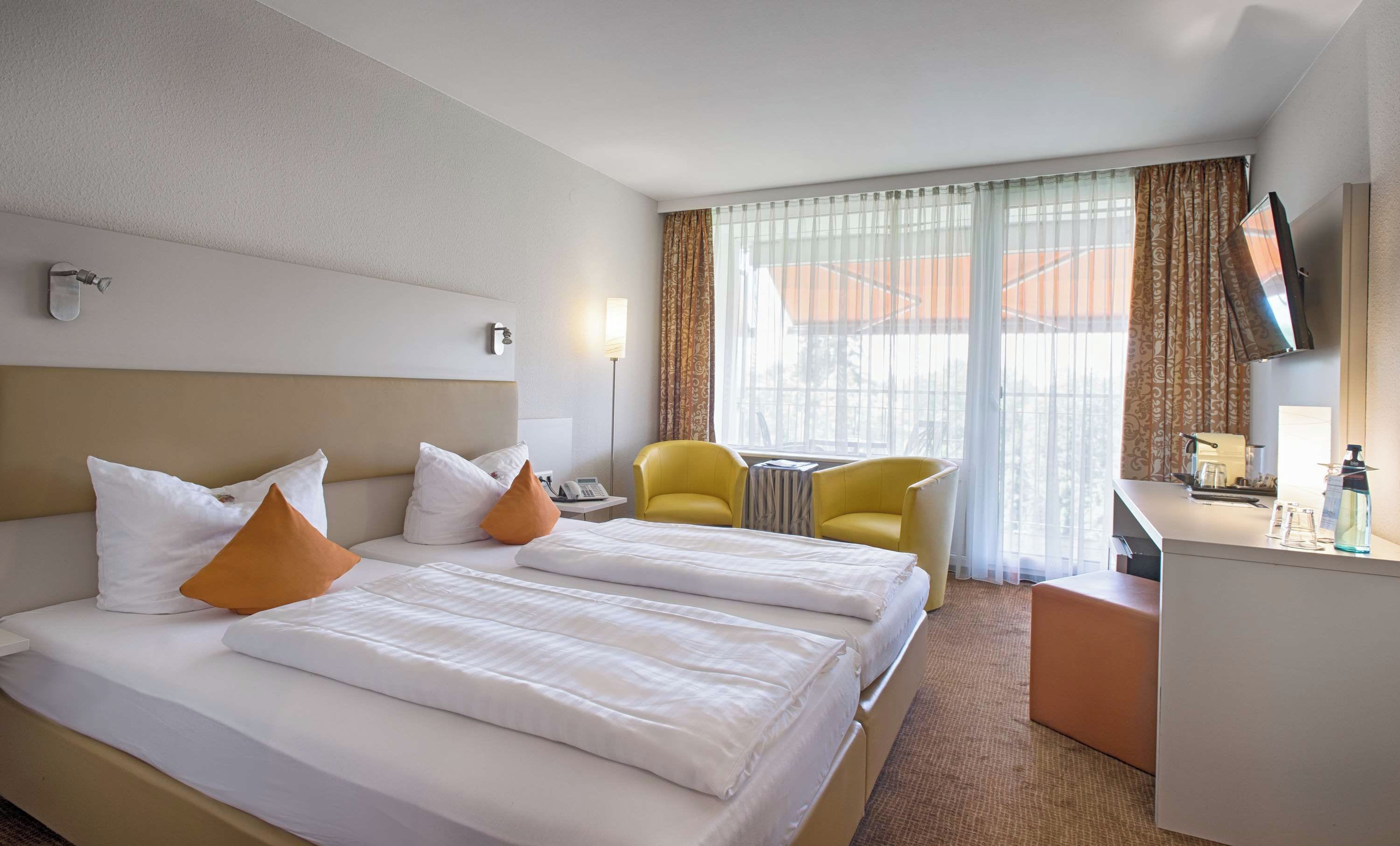 A hotel room with two beds, a desk, a chair, a TV, and a window with curtains.