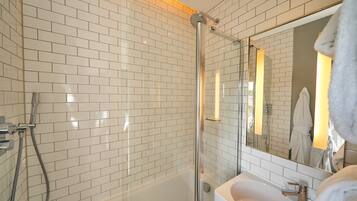 A modern bathroom with white subway tiles, a glass-enclosed shower, a white sink, and a mirror reflecting a robe.