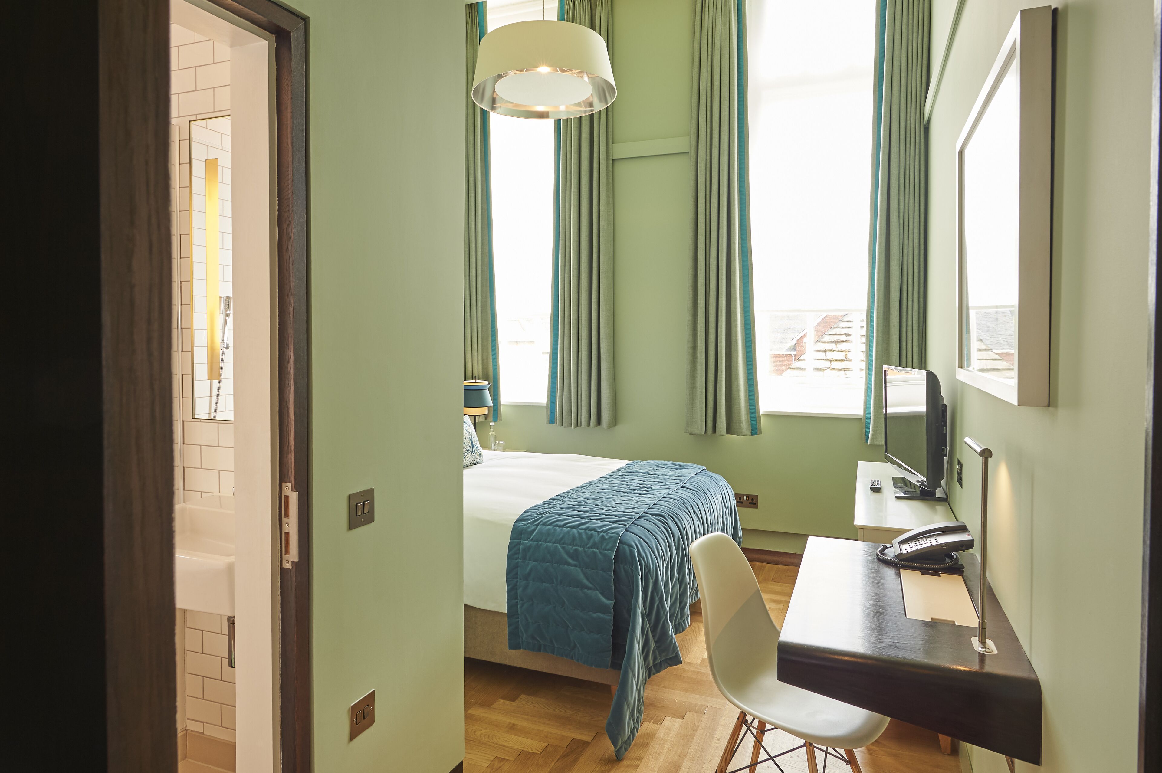 A hotel room with a bed, desk, chair, and a view of the outside.