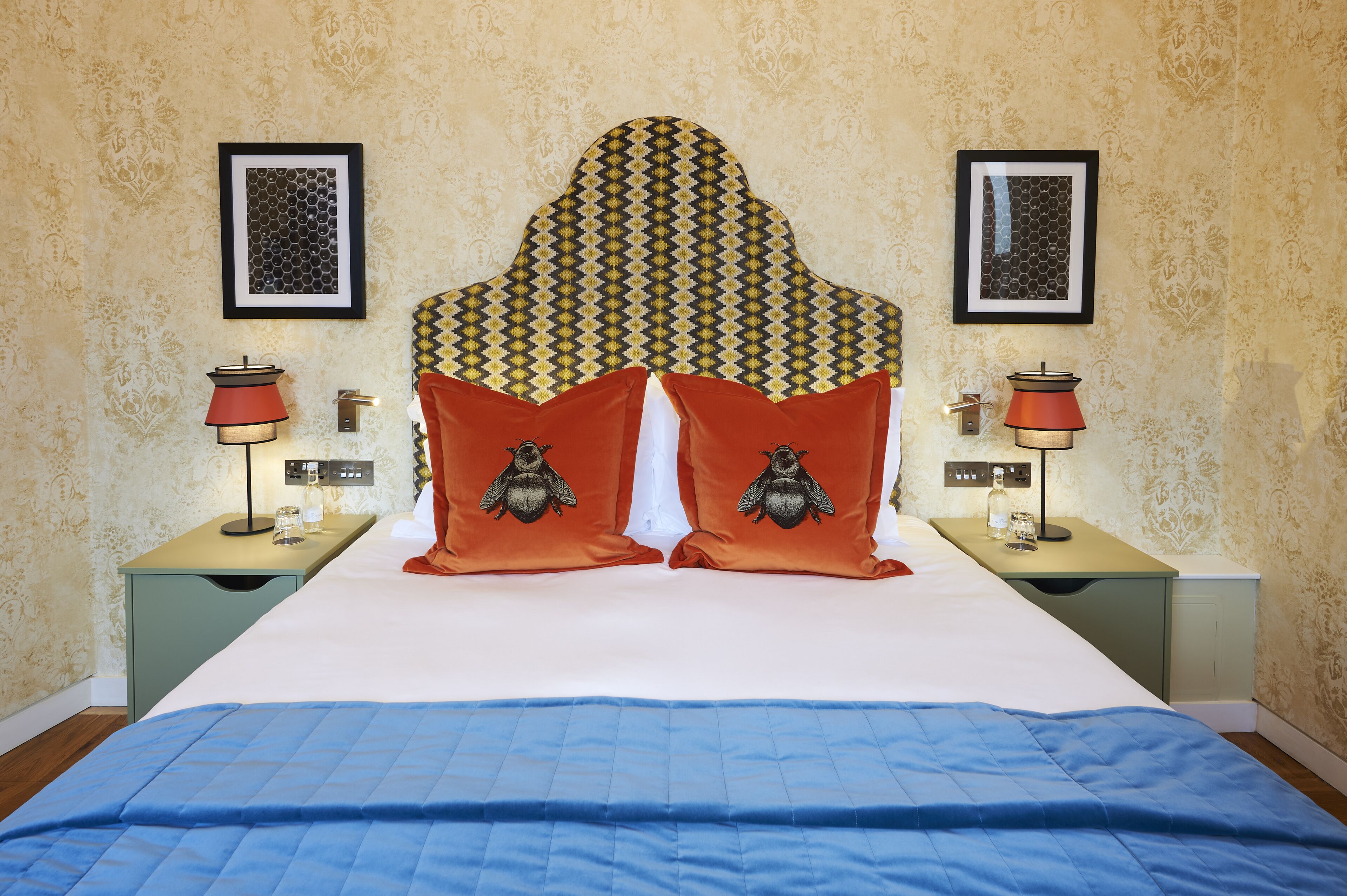 A neatly made bed with a patterned headboard, two nightstands with lamps, and framed pictures on the walls.