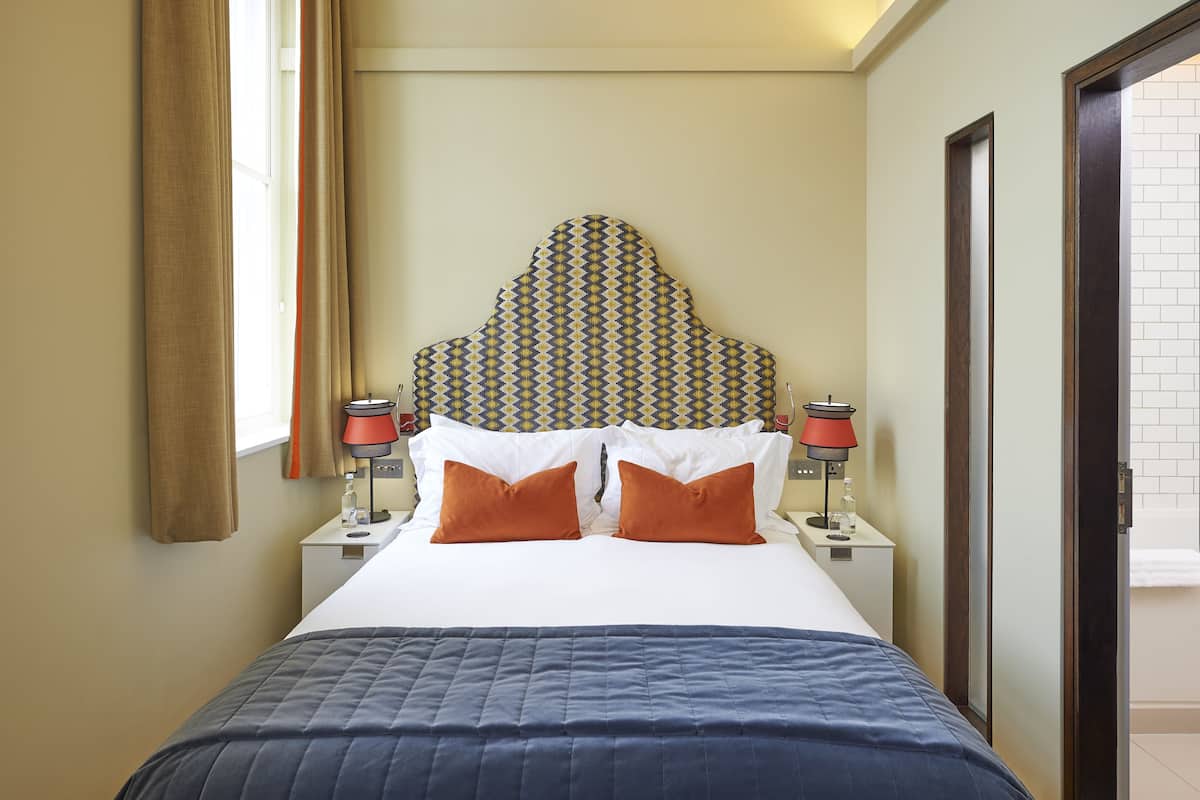 A hotel room with a bed, two nightstands, a patterned headboard, and a window with curtains.