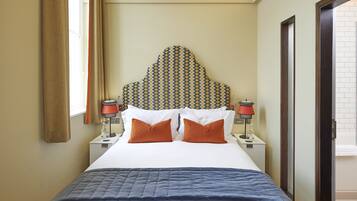 A hotel room with a bed, two nightstands, a patterned headboard, and a window with curtains.