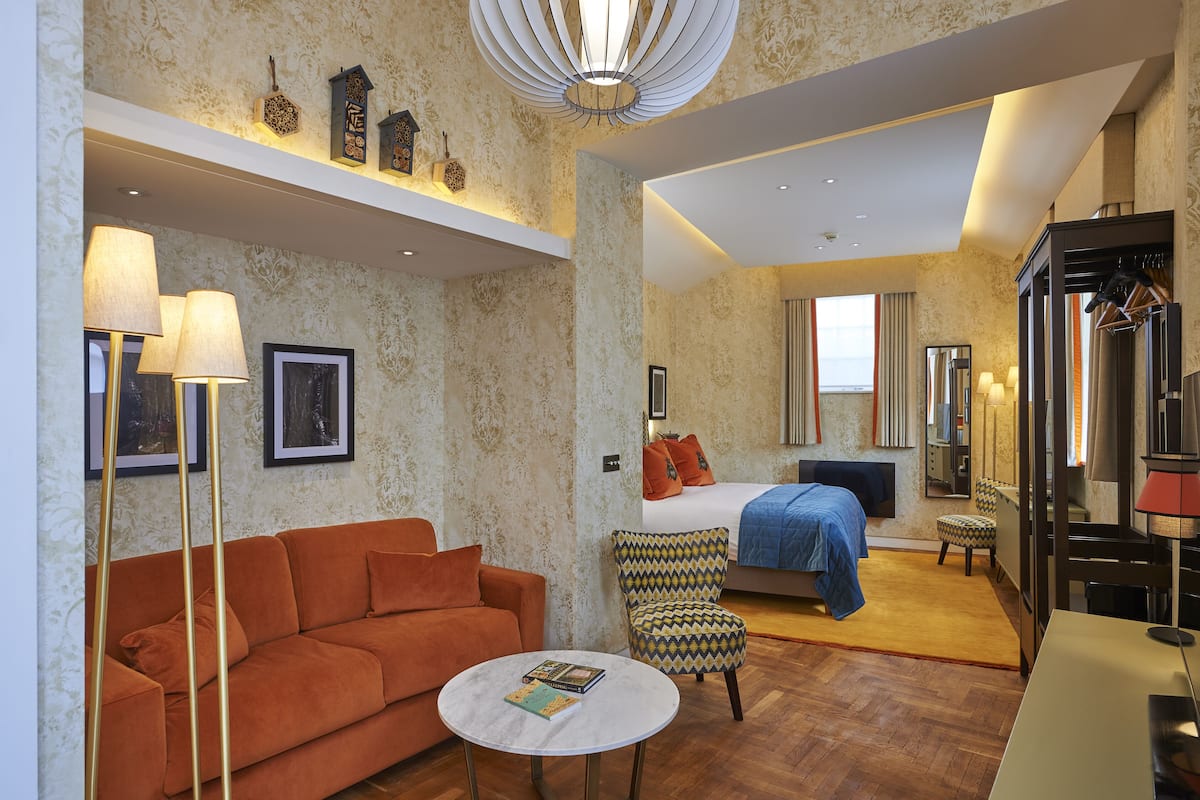 A hotel room with a sofa, armchair, bed, and a small table with a book.