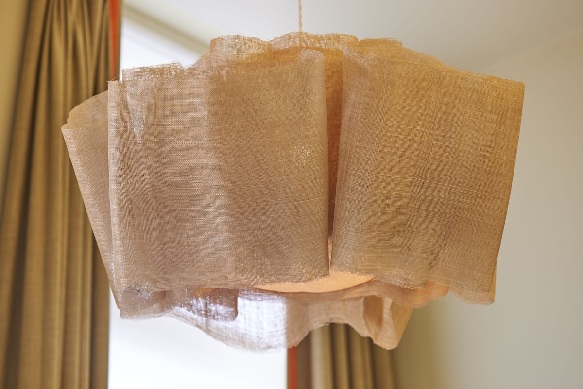 A sheer, beige curtain with a scalloped edge, hanging in a room.