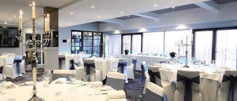 A banquet hall with round tables, white tablecloths, and chairs with black sashes.