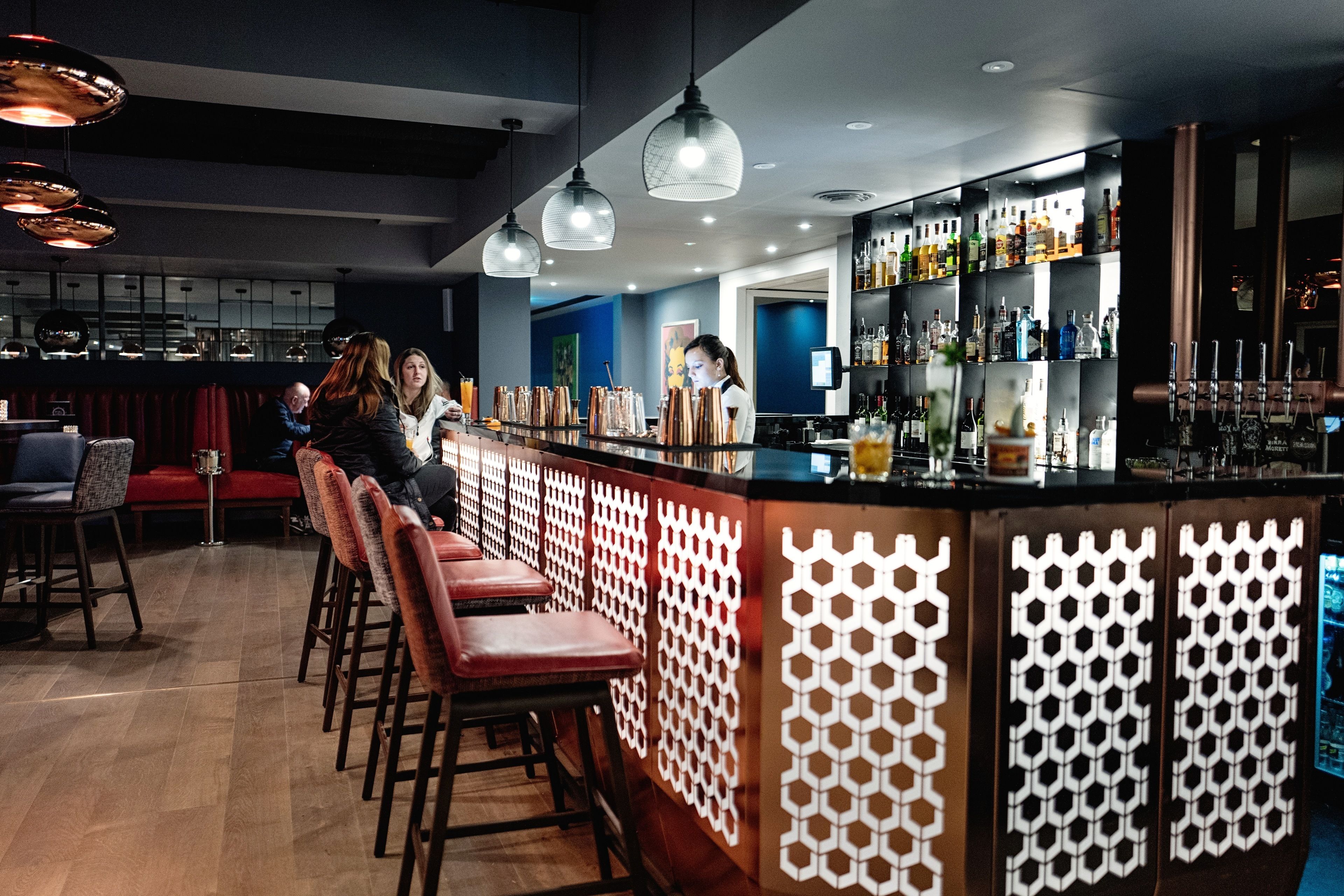 Zona de bar con taburetes de madera, una barra y un barman.