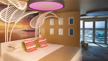 Quarto de hotel moderno com uma cama grande, vista da cidade através de amplas janelas e um design de teto único.