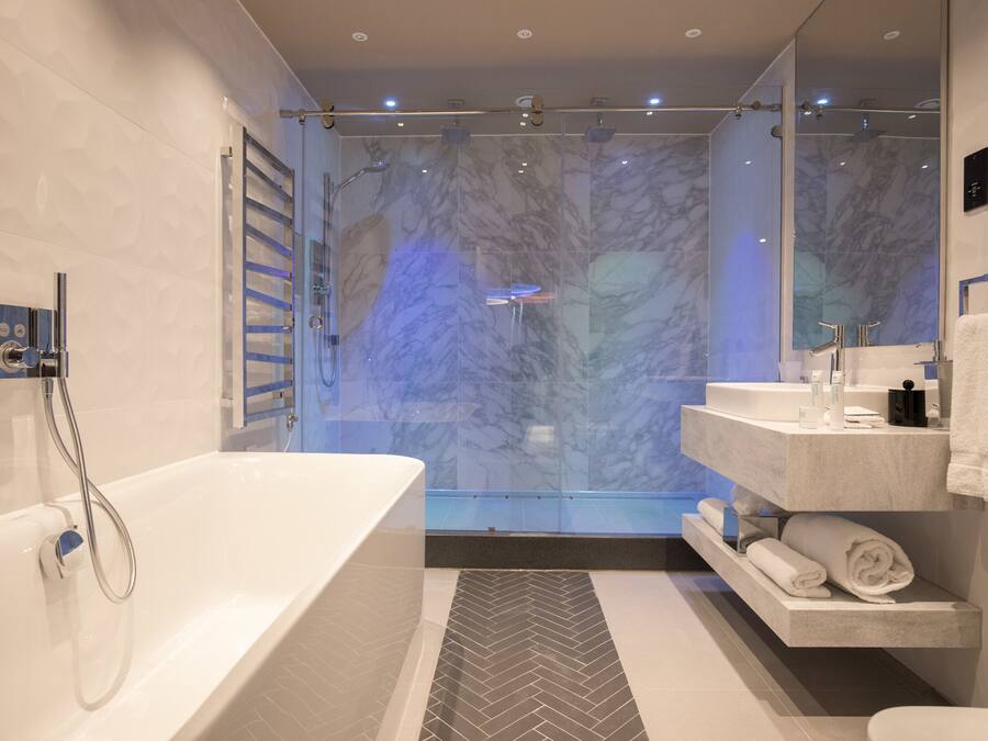 A modern bathroom with a large bathtub, a glass-enclosed shower, and a marble backsplash.